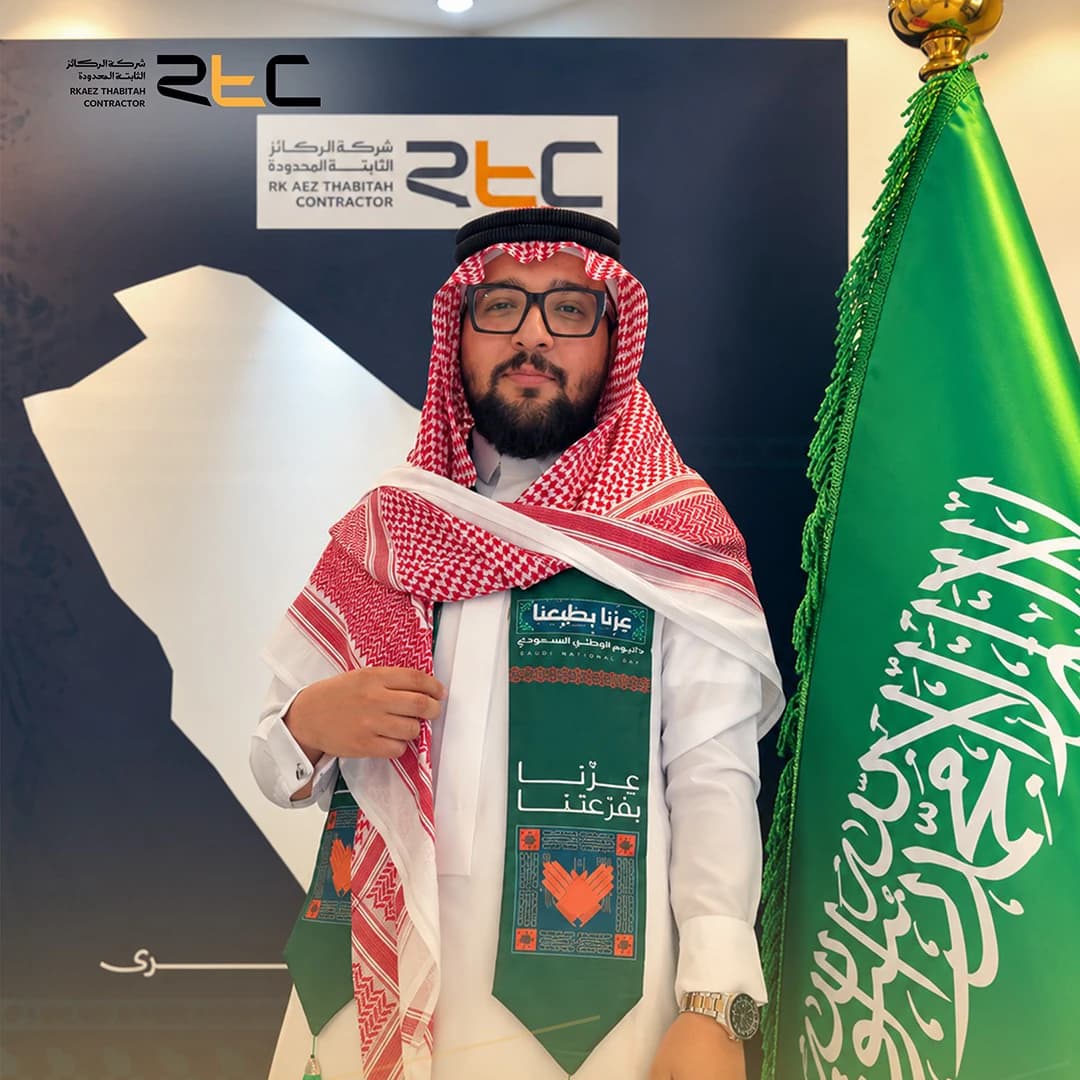 أحد الحضور بالشماغ الأحمر ووشاح اليوم الوطني إلى جانب العلم السعودي