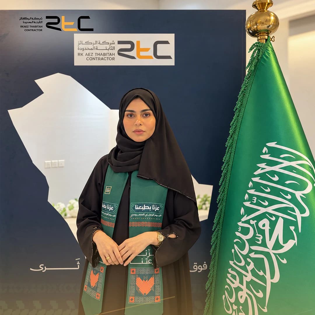 أحد الحضور بعباءة سوداء ووشاح اليوم الوطني أمام خريطة المملكة والعلم السعودي