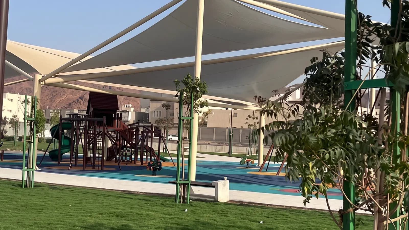 منطقة ألعاب أطفال مظللة بأشرعة بيضاء مع زلاقات وأرضية لعب ملونة بين المسطحات